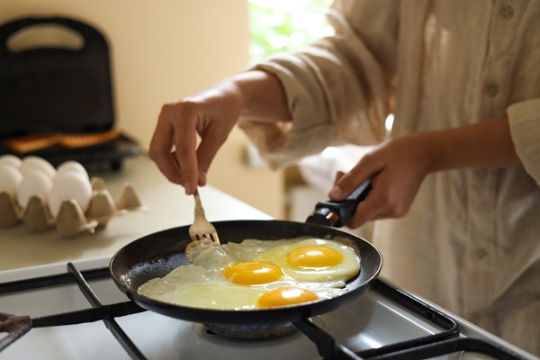 woman cooking tasty eggs on frying pan in kitchen closeup - Диетическая яичница