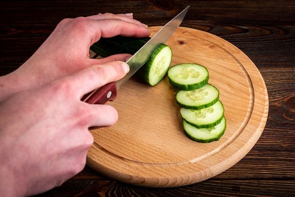 woman hand cutting fresh cucumber on wooden board - Бутерброд с бужениной и огурцом