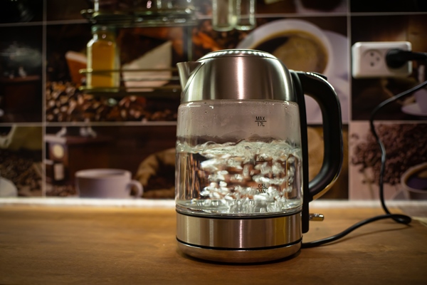 a boiling electric kettle stands on a brown table the kettle is plugged in a transparent kettle boils in the evening kitchen - Сладкий квас