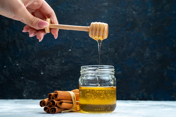 a front view honey and cinnamon female dunking spoon into the honey on the blue grey background sugar plant - Красносельский квас