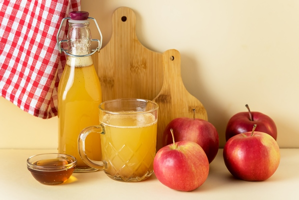 apple cider vinegar in glass mug and bottle with honey and cinnamon red apples yellow background - Осенний квас