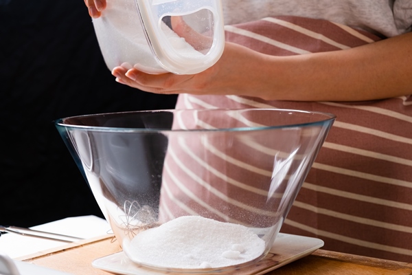 close up woman pouring flour into a mixing bowl for preparation of pastry dough on the black backgro - Гречнево-ржаной хлеб