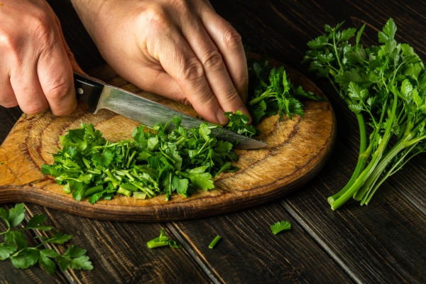 cook cutting green parsley on a cutting board with a knife for preparing a vegetarian dish - Суп с помидорами