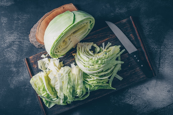 flat lay sliced and chopped cabbage in cutting board and knife with wood stub on dark textured background horizontal - Щи из свежей капусты постные