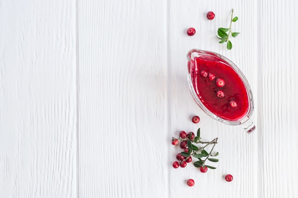 fresh lingonberry sauce in a gravy boat on a white wooden background top view with copy space - Драники с яблоками и брусникой