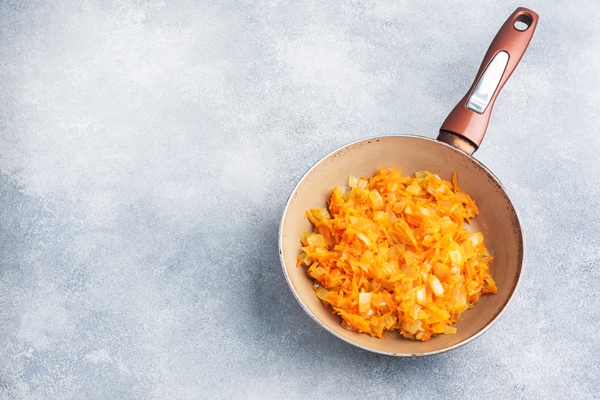 fry grated carrots and chopped onions with oil in a frying pan gray concrete background copy space - Постная грибная лапша с вермишелью