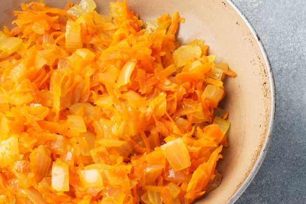 fry grated carrots and chopped onions with oil in a frying pan gray concrete table copy space - Суп картофельный с бобовыми