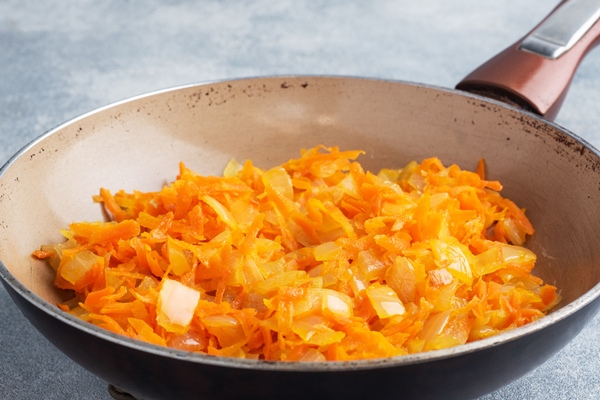 fry grated carrots and chopped onions with oil in a frying pan gray concrete - Рисовый суп с грибами