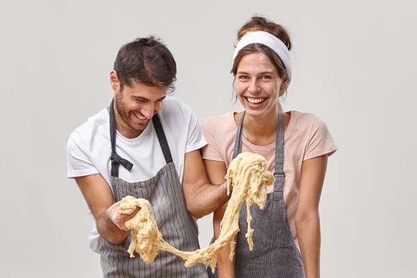 funny man wears apron tries to cook pastry stretches sticky dough has cooking failure cheerful housewife stands near surrounded with baking products on table try cookies recipe pose at kitchen - Чиабатта