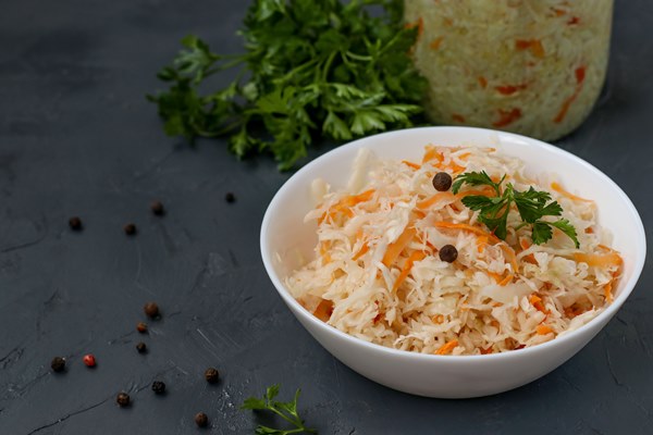 homemade sauerkraut with carrots and parsley in a bowl and jar on a dark background fermented food closeup copy space - Постный борщ с грибами и квашеной капустой