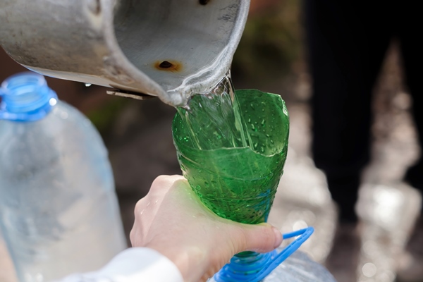 man using scoop and funnel drawing water from well - Уборочный квас