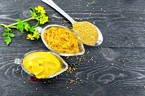 mustard sauce and dijon mustard in two glass saucepans yellow flower and seeds in a spoon on the background of wooden board from above - Окрошка со сливами