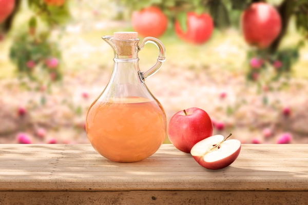 organic apple cider vinegar in glass jug on rustic wooden table apple orchard in background - Арбатский квас