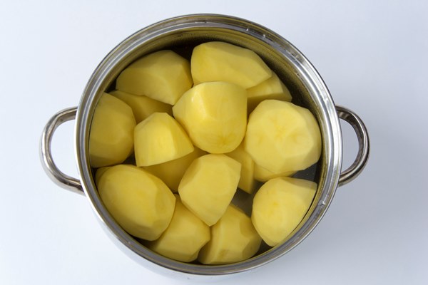 peeled sliced potatoes lie in water in a saucepan ready to cook on the stove - Драники с мочёной брусникой