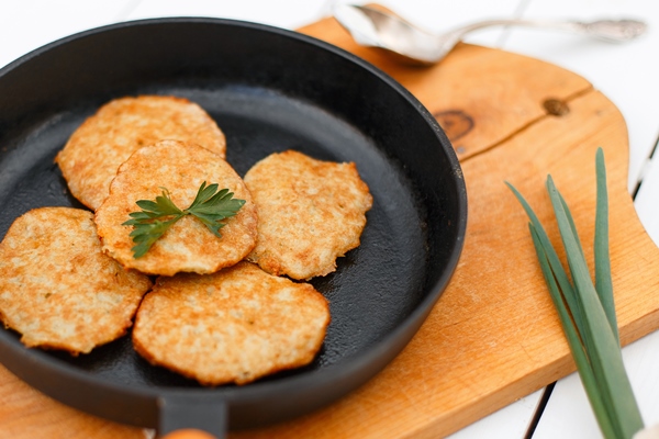 potato pancakes on a cast iron frying pan with onions on a white wooden table - Драники с добавлением соды