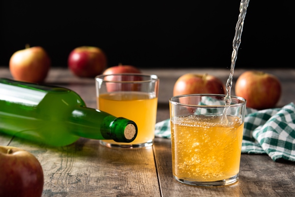 pouring apple cider drink into a glass on wooden table - Яблочный квас (сидр)