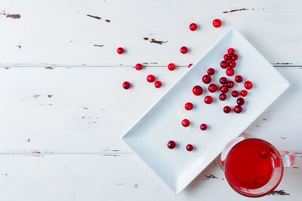 selective focus on cranberries in a fresh drink in a glass cup on a white wooden background fresh ripe berries are scattered on a white rectangular ceramic plate copy space flat lay - Питерский квас