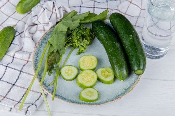 side view of vegetables as whole and sliced cucumber spinach coriander with cucumbers on cloth and detox water on wooden table - Ботвинья (способ второй)