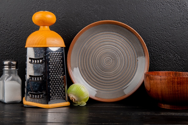 side view of white onion with salt grater bowl and plate on wooden surface and black background - Драники с зеленью