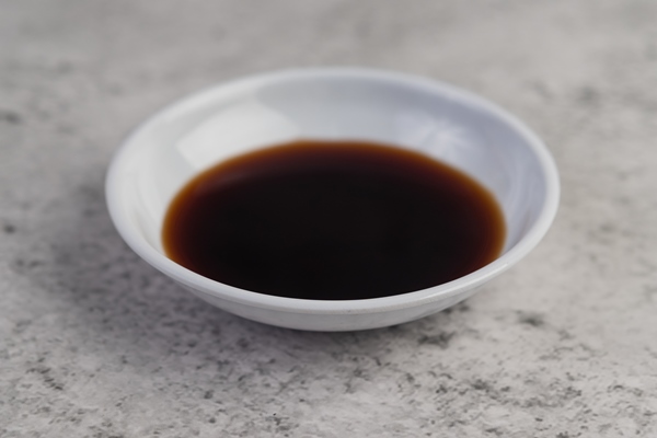 the black sauce in a small white cup placed on the cement floor - Квас яблочный скороспелый