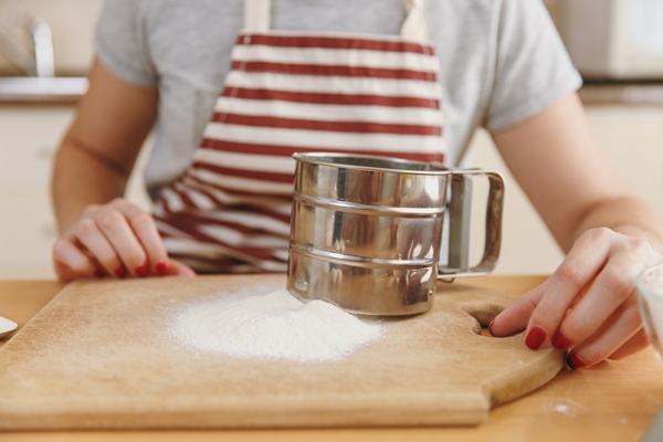 the close up shot of the young woman in apron with iron sieve and flour on the table in the kitchen cooking home prepare food - Финский овсяный хлеб