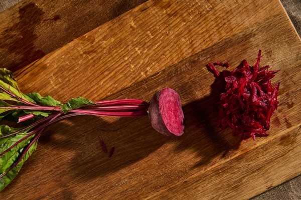 top view of fresh juicy raw burgundy beetle with tops half shredded on a grater on a wooden kitchen board flat lay food background - Квас из свёклы