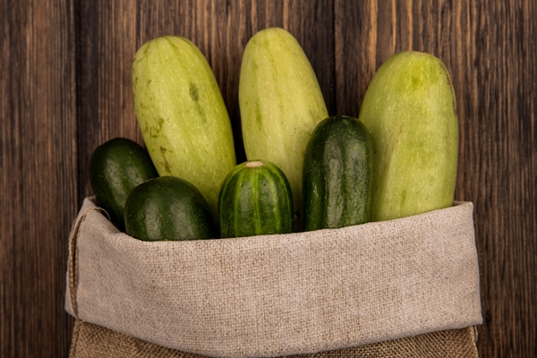 top view of fresh vegetables such as cucumbers and zucchinis on a burlap bag on a wooden wall - Драники с кабачками и луком