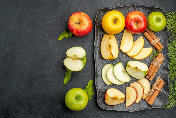 top view of green yellow and red sliced and whole fresh apples on a black tray and cinnamon on a dark background - Смоленский квас