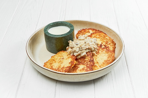ukrainian potato draniki or hash browns in a plate on a white wooden background - Драники с шампиньонами