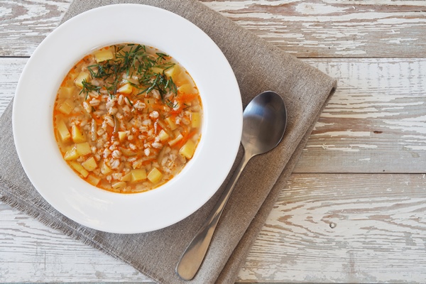 vegetable soup with cereals and pickles in a white bowl on rustic wooden table - Суп перловый с репой