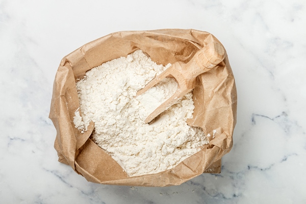 wheat flour and a wooden scoop in a paper bag on a marble table bakery concept - Драники с кабачками