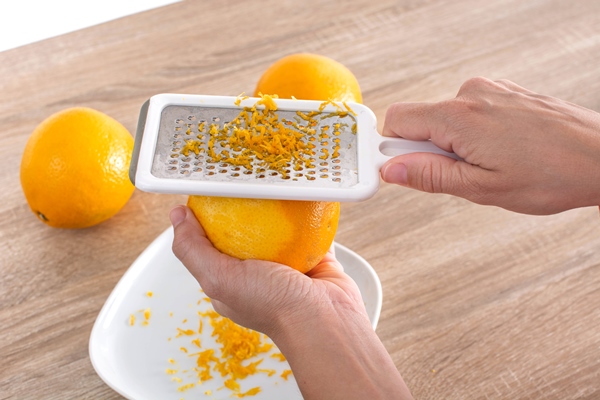 woman rubbing orange zest with metal grater in the kitchen - Тамбовский ревеневый квас