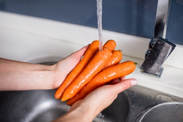 woman washing carrots at kitchen washbasin - Рассольник с рисом