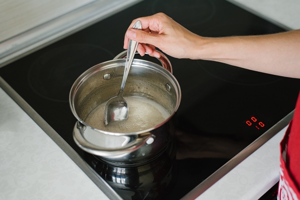 a woman s hand stirs the sugar syrup liquid in a saucepan on an electric stove with a tablespoon - Мочёные яблоки в банках