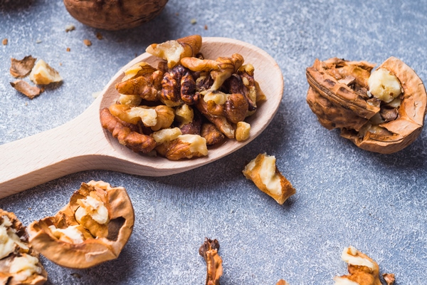 close up of walnut kernel on wooden spoon - Слоёный салат с шампиньонами и черносливом