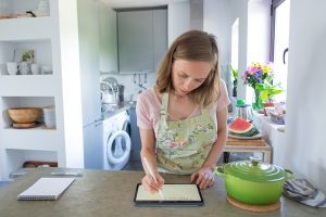 focused young woman planning weekly menu writing on pad screen while cooking in her kitchen using tablet near big saucepan on counter front view cooking at home and household concept - Правила составления меню