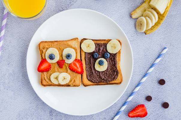 healthy funny face sandwiches for kids animal faces toast with peanut and hazelnat chocolate butter banana strawberry and blueberry on a white plate with orange juice close up top view - Сказочные бутерброды