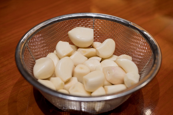 peeled garlic in a stainless steel collander on a wood surface with selective focus point - Постная яблочная аджика с базиликом