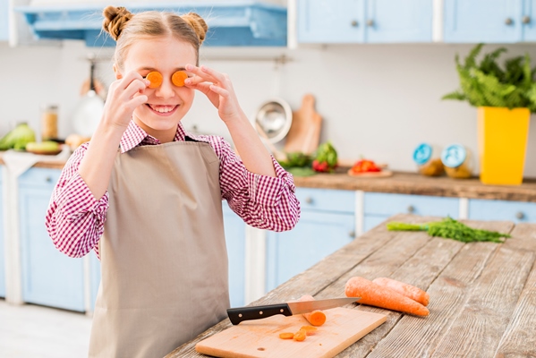 portrait of a girl covering his eyes with carrot slice in the kitchen - Зелёный суп