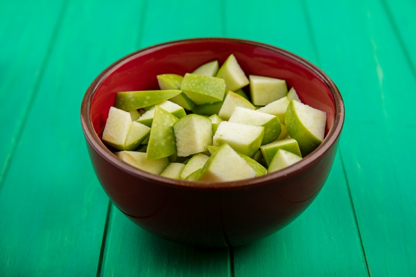 side view of chopped apples on red bowl on green surface - Замороженные яблоки на зиму