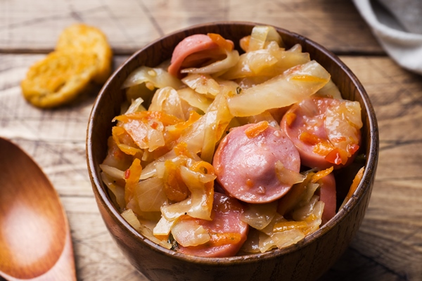 stewed cabbage with sausages in wooden bowls on the table - Сосиски или сардельки отварные