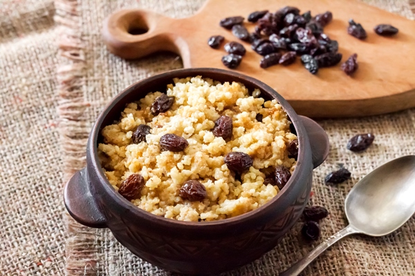 sweet millet porridge with dark raisins in ceramic rustic bowl on sackcloth background - Пшённая каша с изюмом или черносливом
