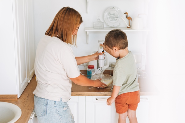 young woman mother and her toddler boy son cooking with blender at table in bright kitchen at home - Как правильно учить детей готовить?