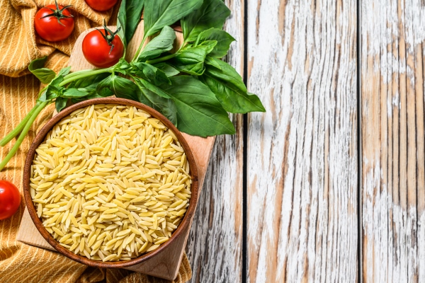 a bowl of raw orzo pasta with basil leaves tomatoes and garlic - Минестроне, постный стол