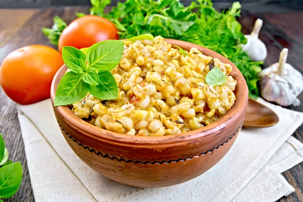 barley porridge in a clay bowl with basil on towel tomatoes parsley and garlic on a wooden boards background - Лечебный стол (диета) № 4 по Певзнеру: таблица продуктов и режим питания