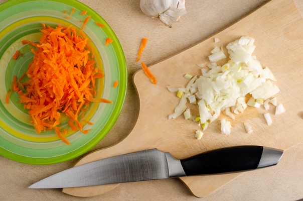 chopped onion on a wooden cutting board and grated carrot on the plate and knife - Постный картофель, тушённый с фасолью