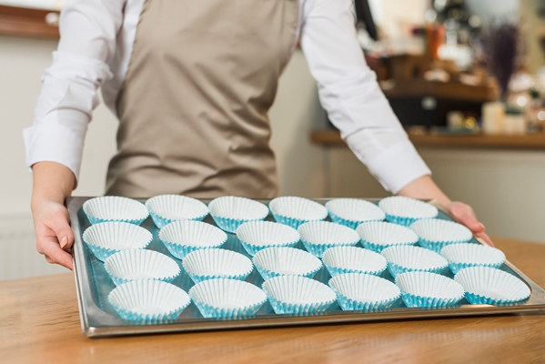 close up of female baker holding baking stainless tray with arranged cupcake silicon molds - Постный грибной крамбл