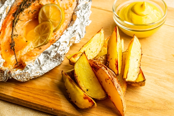 close up of the fresh fried potatoes on the wooden cutting board and mustard near fish in foil - Сёмга, запечённая с луком и картофелем, постный стол