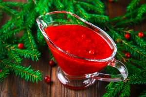 cowberry cranberry sauce in a glass clear saucer on a wooden table with spruce branches - Яблоки, запечённые с начинкой