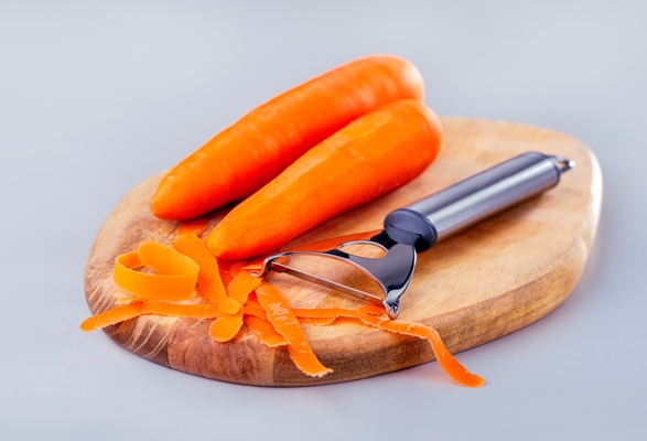 fresh carrot with peeler at wooden board on grey background banner design vegetables for a healthy diet - Баклажанные рулетики с морковью